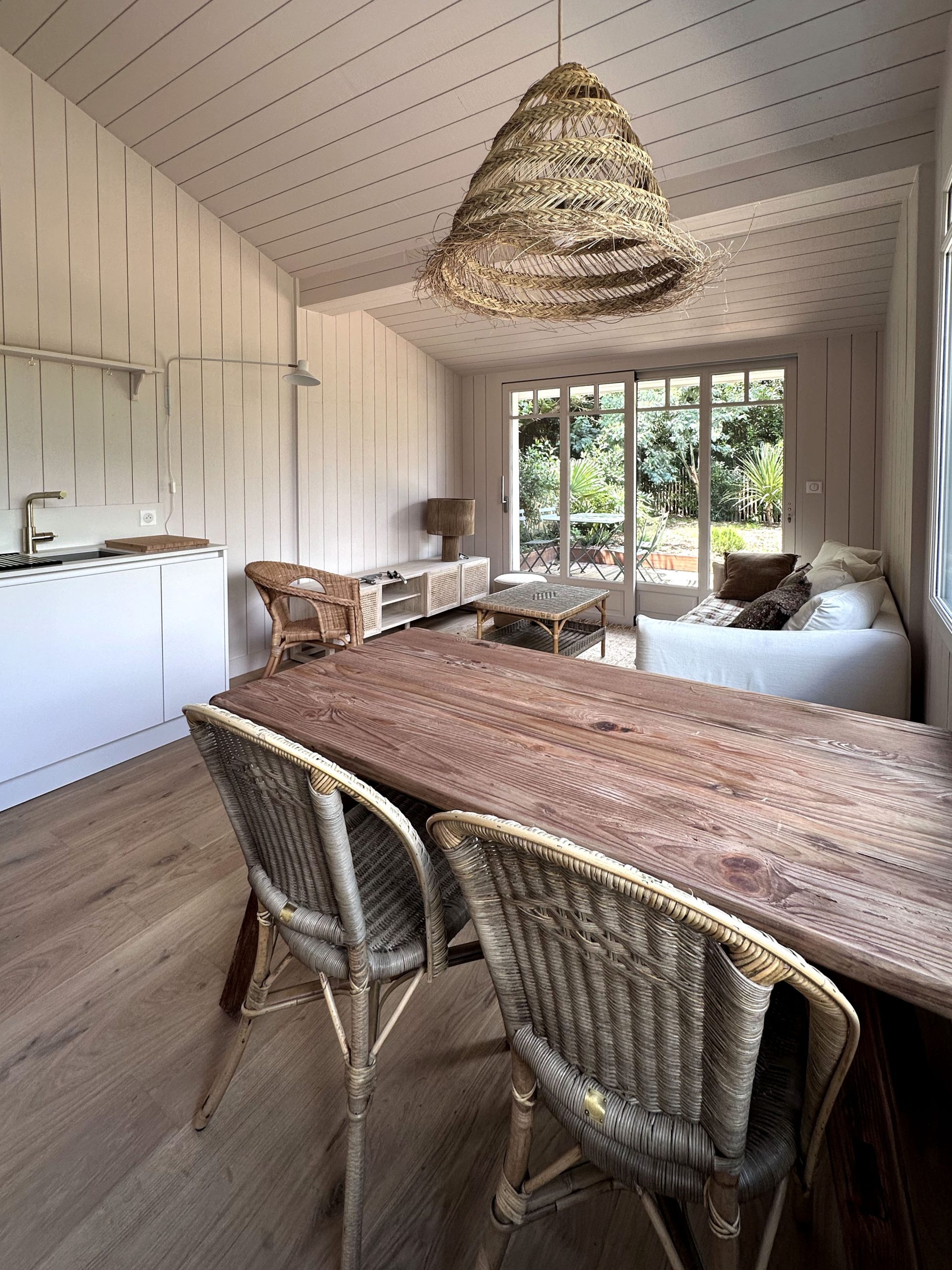 Tavolo in legno con sedie in vimini davanti a grandi finestre nella casa vacanze a Cap Ferret con cucina Zecchinon di Quartier Cuisine