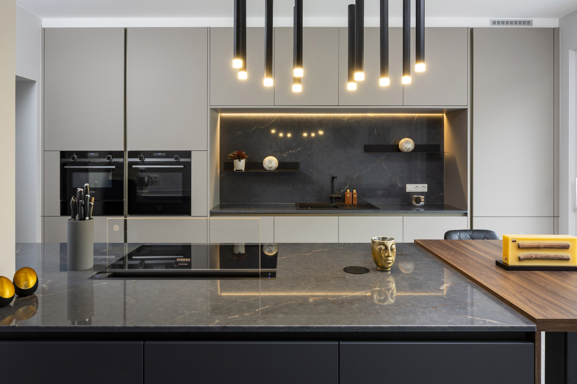 Cucina moderna su misura con isola in effetto pietra antracite, mobili senza maniglie in finitura Sandalo opaco, piano colazione in laminato Wood Noce e illuminazione LED integrata