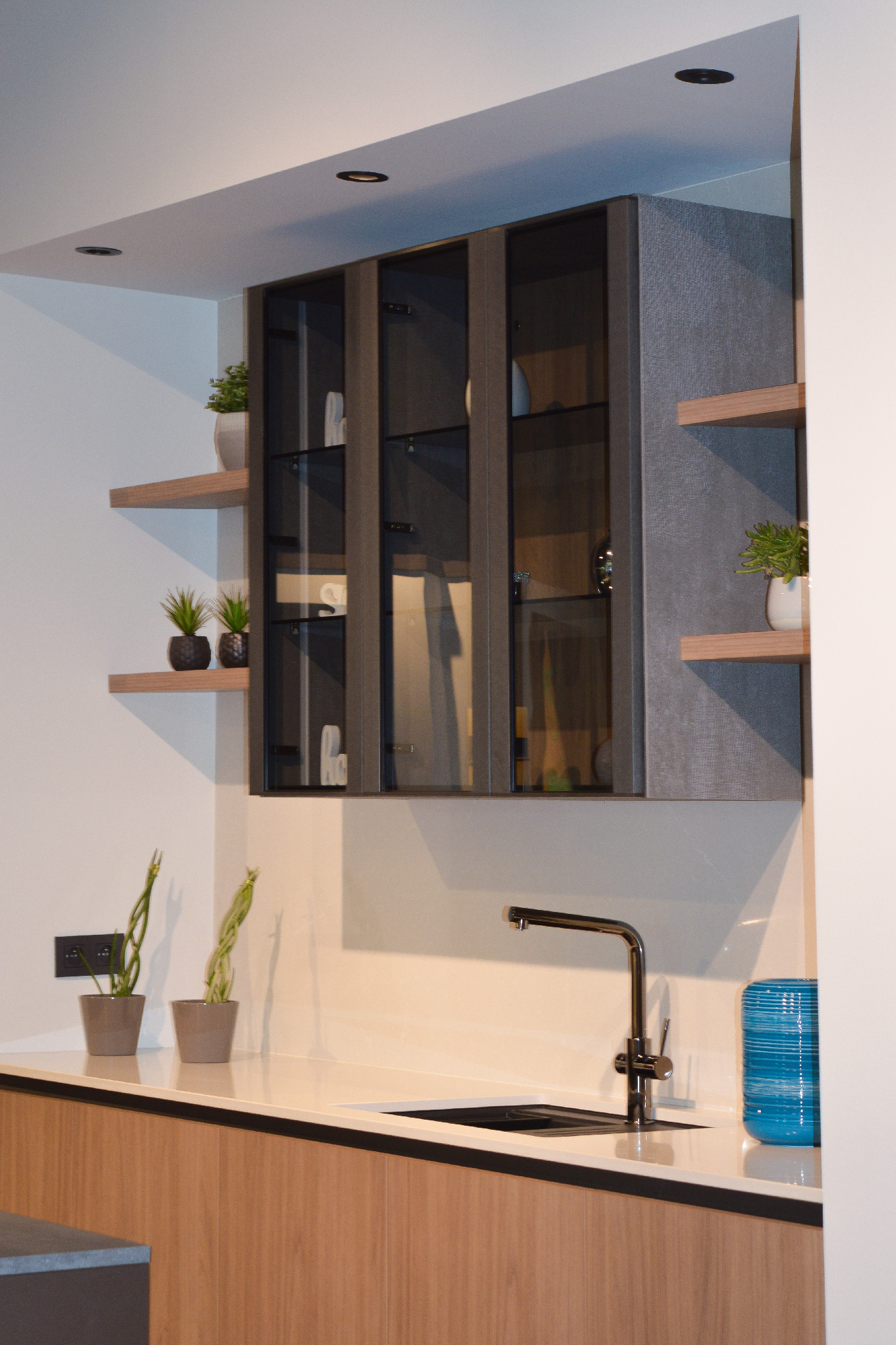 Cucina con lavello sottotop e rubinetto cromato, pensili in vetro fumé, mensole in legno chiaro e dettagli decorativi in stile minimal.