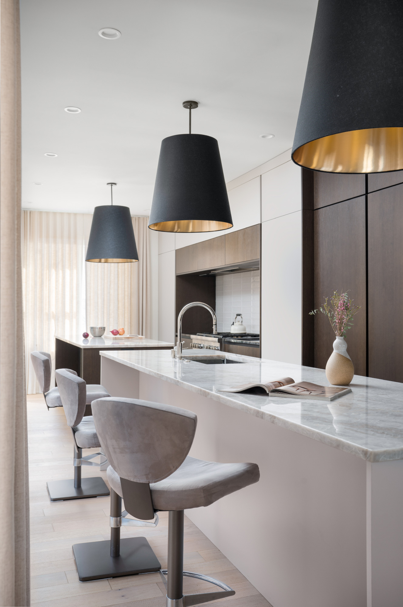 Cucina contemporanea con doppia isola in marmo chiaro, sgabelli in velluto grigio e grandi lampade nere a sospensione con interno oro ramato. Progetto Zecchinon e Archisesto a Chicago.