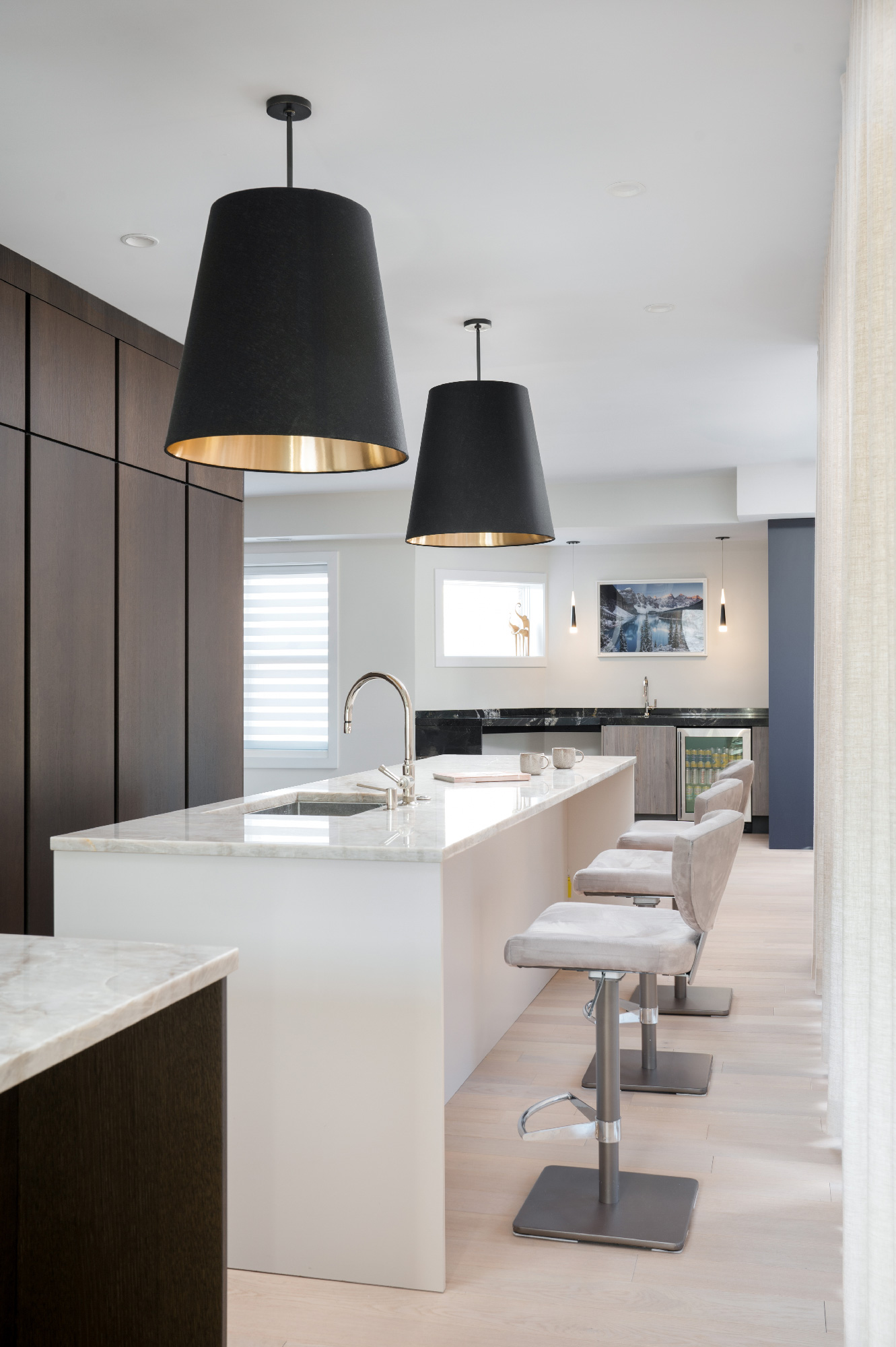 Dettaglio frontale di isola cucina con top in marmo, sedute imbottite e sfondo con pensili in legno scuro, backsplash bianco lucido e lampada nera con interno dorato. Progetto Zecchinon e Archisesto a Chicago.
