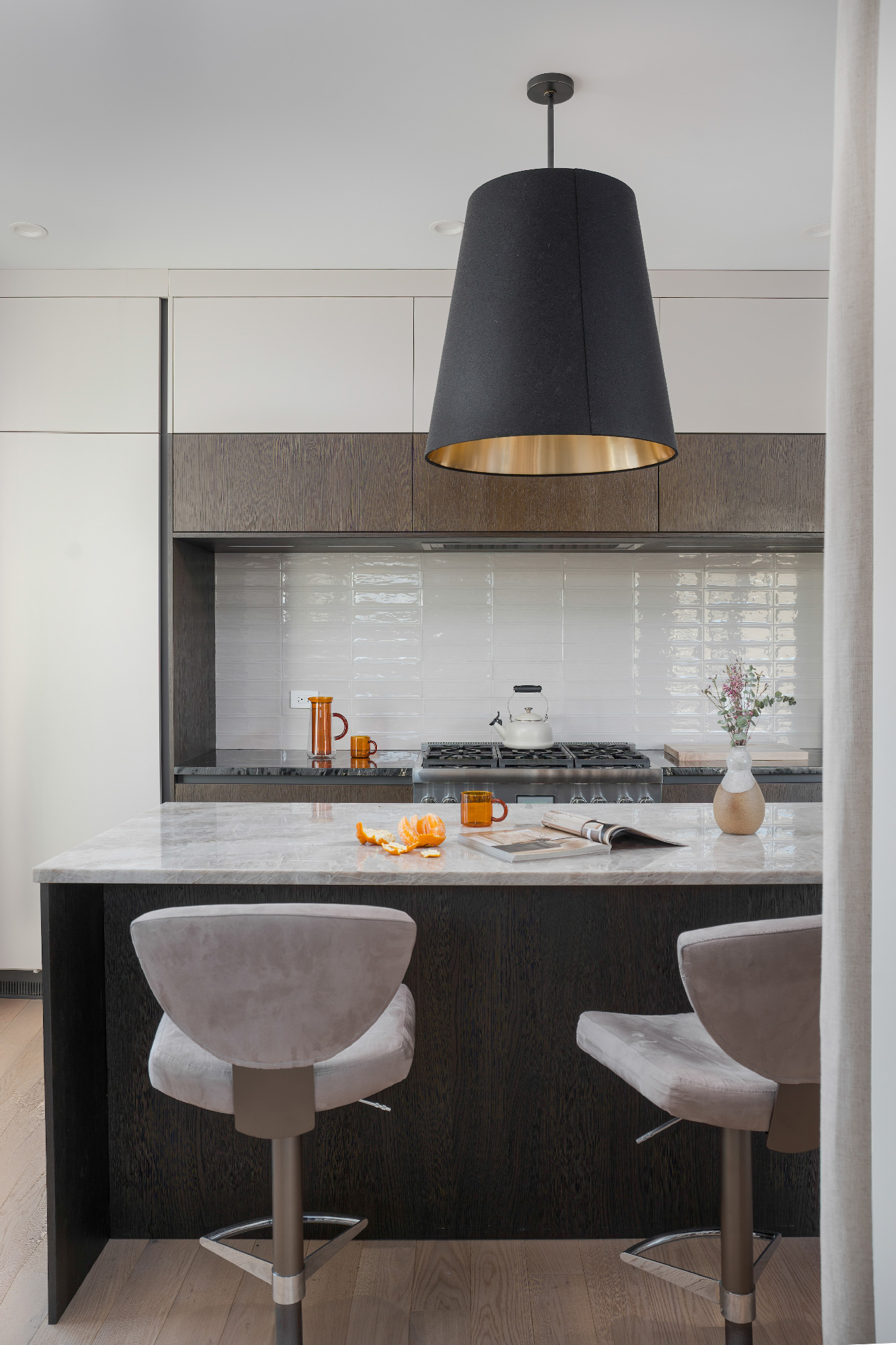 Cucina moderna con isola lunga e linee minimaliste, sgabelli grigio perla e grandi sospensioni nere, vista su zona living con luce naturale. Progetto Zecchinon e Archisesto a Chicago.