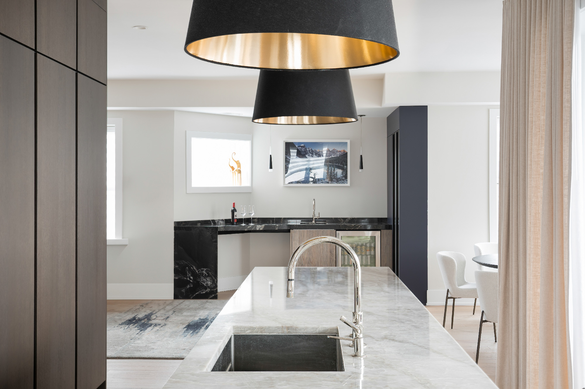 Primo piano su lavello da cucina con rubinetto inox e piano in marmo, in ambiente con controsoffitto moderno e angolo bar con cantinetta integrata. Progetto Zecchinon e Archisesto a Chicago.