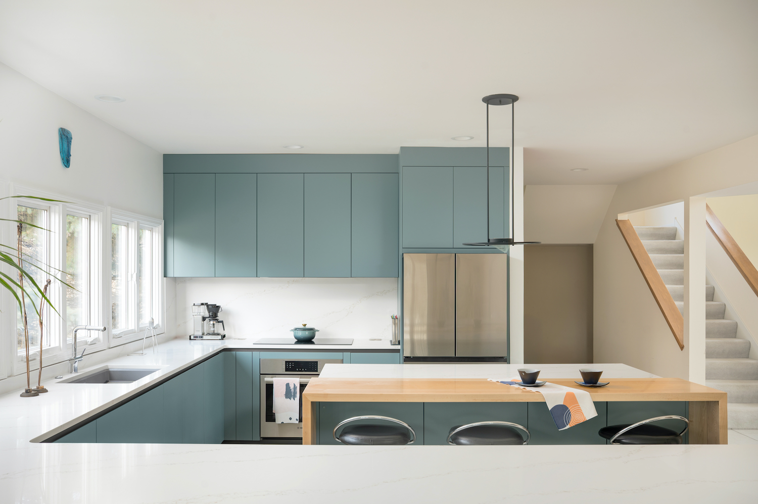 Cucina in laccato opaco con pensili e isola centrale con inserto in legno per la zona colazione e piano a induzione. Illuminazione a sospensione sopra l'isola cucina