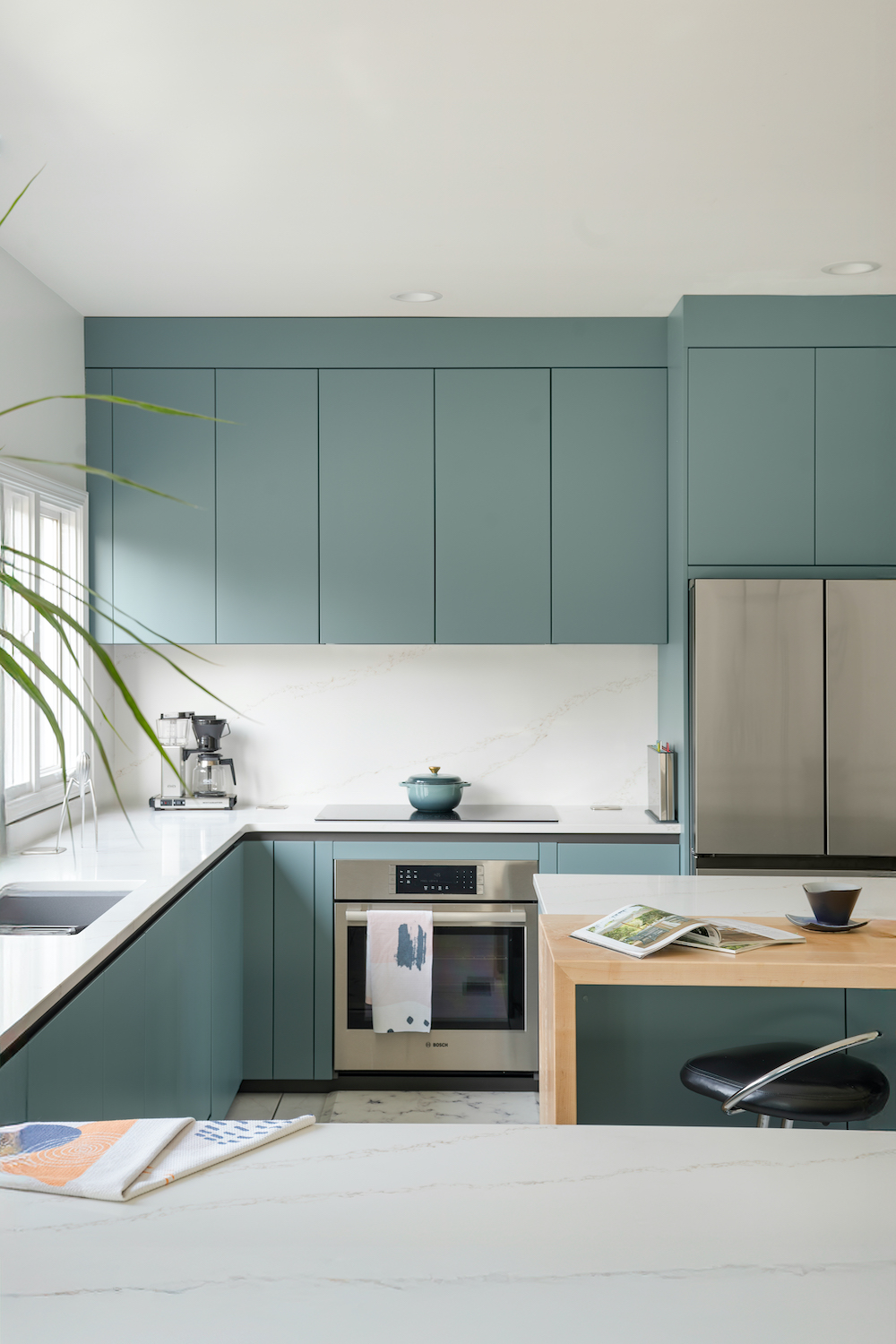 Cucina in laccato opaco con pensili, frigo e forno in acciaio, isola centrale con inserto in legno e illuminazione moderna a sospesione
