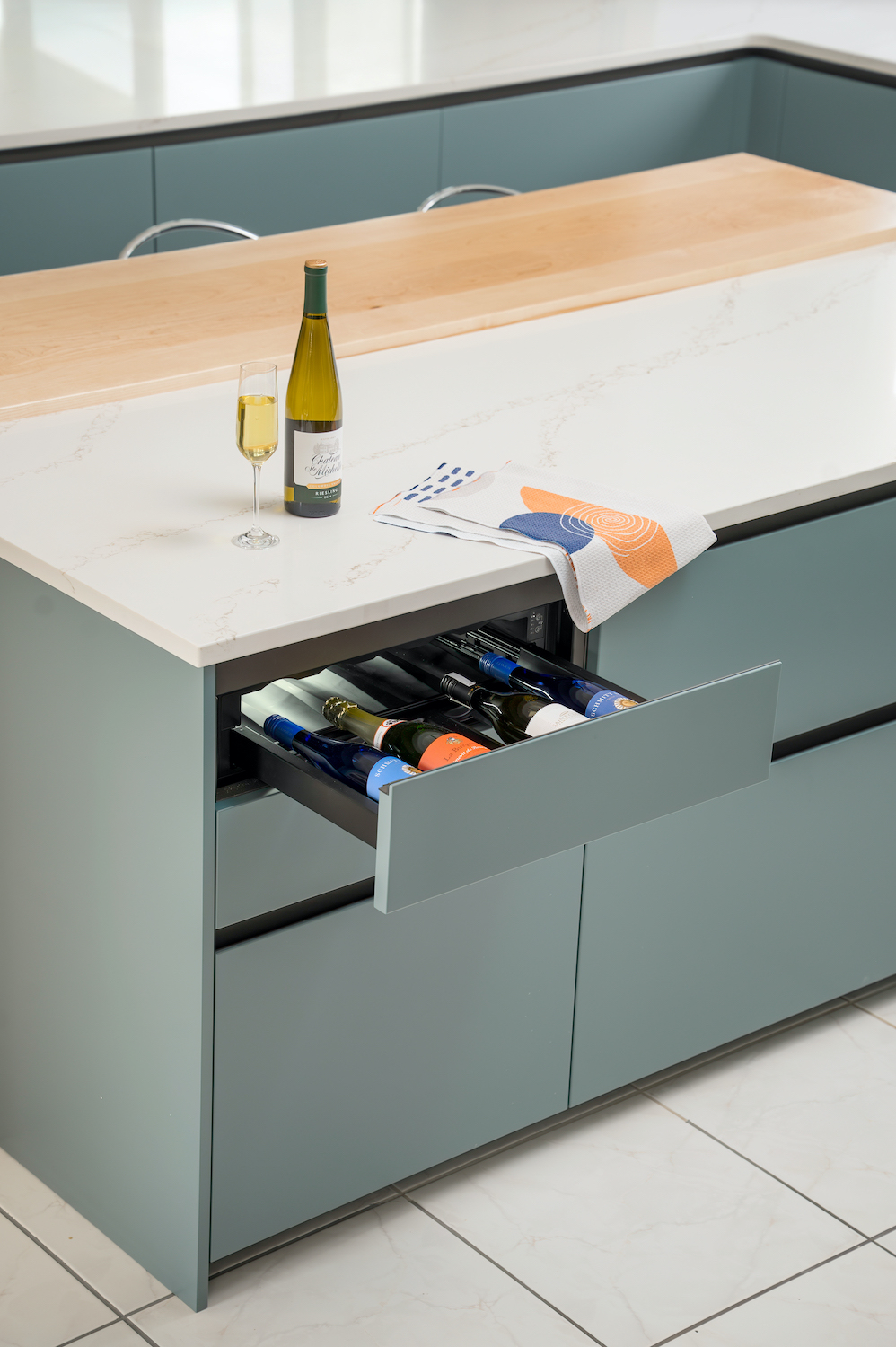 Isola cucina in laccato opaco con cassetto aperto contenente 4 bottiglie di vino.